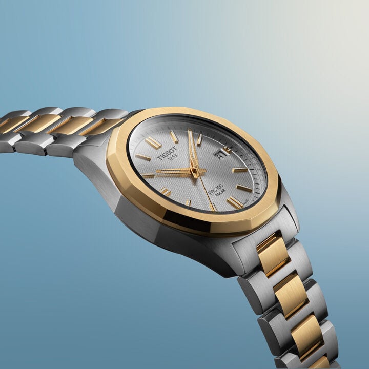 Eine gelbgold-bicolorfarbene Tissot PRC 100 Solar 34mm Damenuhr vor einem hellblauen Hintergrund.