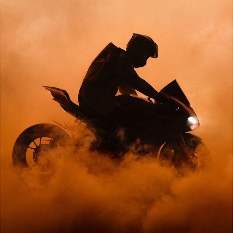 Visual de campa&ntilde;a que muestra una motocicleta en una nube de polvo naranja.