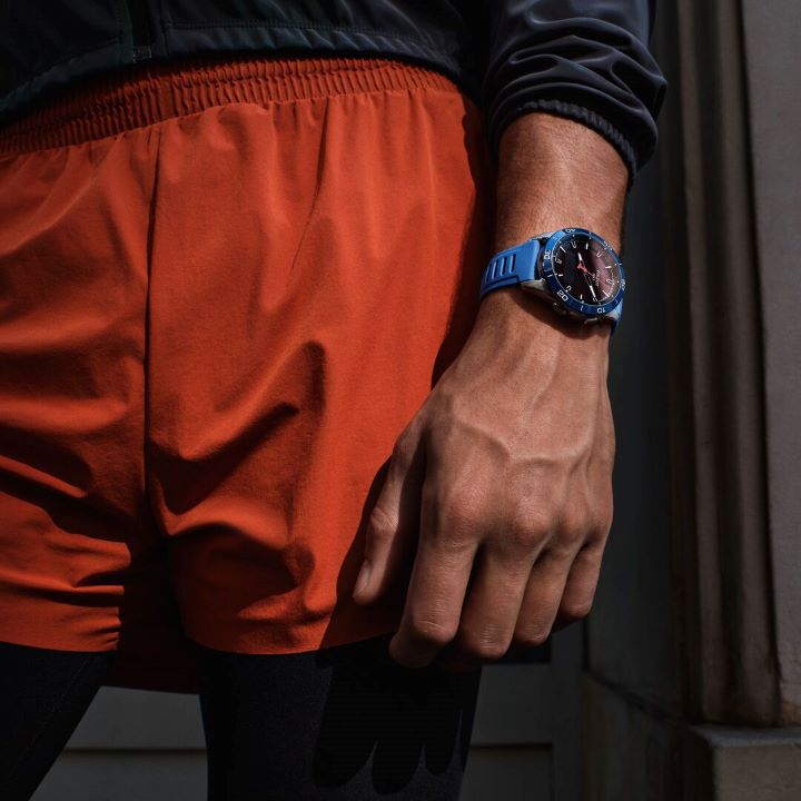 Homme portant un short de sport orange et la version bleue de la montre Tissot T-Touch Connect Sport &agrave; son poignet.