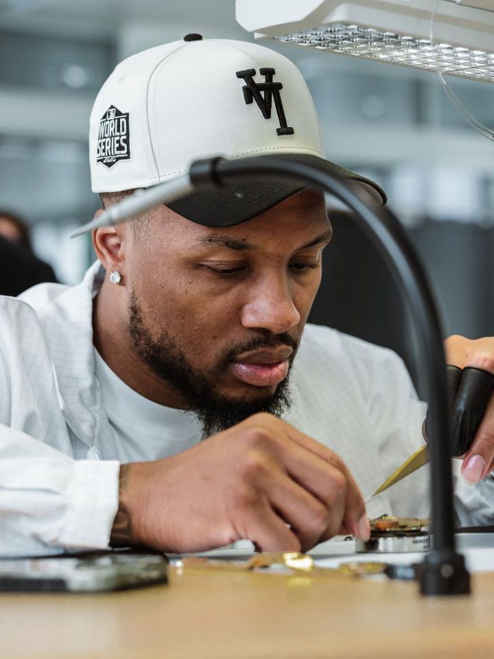NBA Superstar Damian Lillard, portant une casquette blanche et un blouson blanc manipulant des outils de pr&eacute;cision horlogers travaillant sur un mouvement de montre de la marque Tissot.