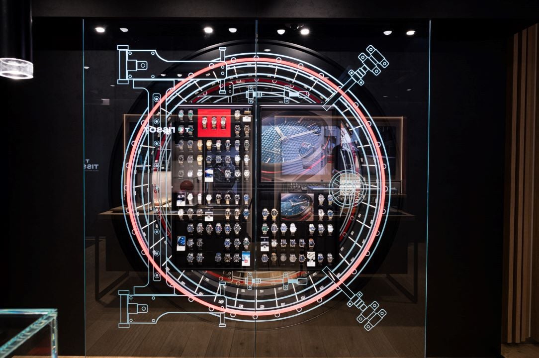 Eine Wand mit einem detaillierten Diagramm eines Uhrwerks, das eine große Auswahl an Tissot-Uhren zeigt, die ordentlich angeordnet sind.