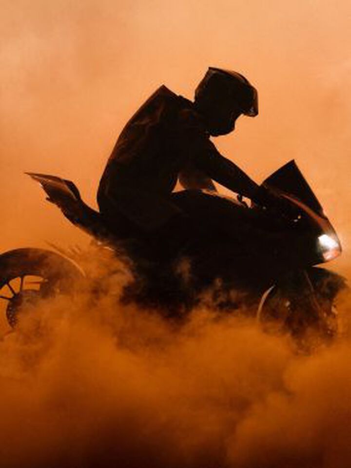 Visual de campa&ntilde;a que muestra una motocicleta en una nube de polvo naranja.