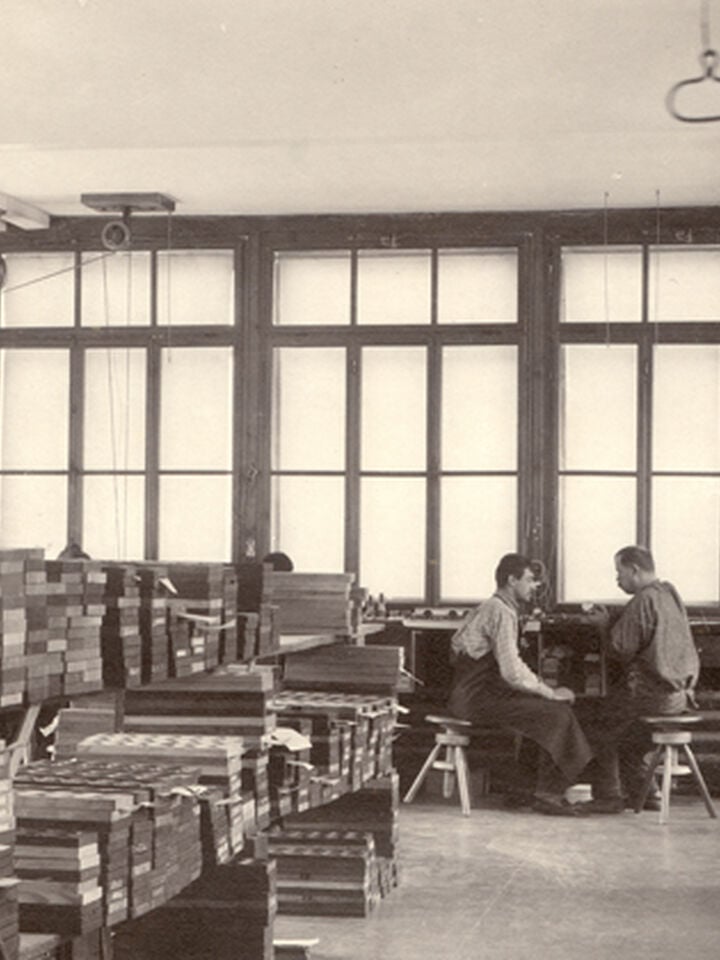 Atelier de finition de montres Tissot au d&eacute;but des ann&eacute;es 1900 &agrave; Le Locle, avec des ouvriers assemblant des composants et des machines entra&icirc;n&eacute;es par courroie au-dessus.