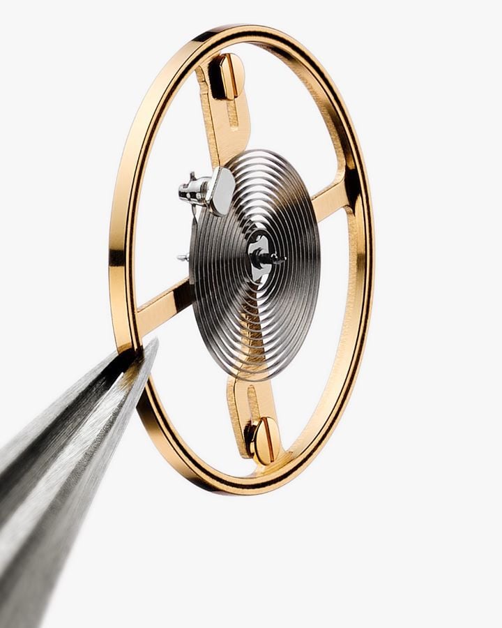 Primer plano del balance del movimiento Powermatic 80 de un reloj Tissot, con resorte espiral y caja circular dorada.