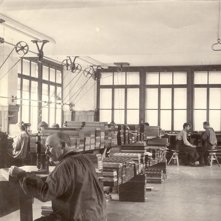 Early 1900s Tissot watch finishing workshop in Le Locle, with workers assembling components and belt-driven machines overhead.