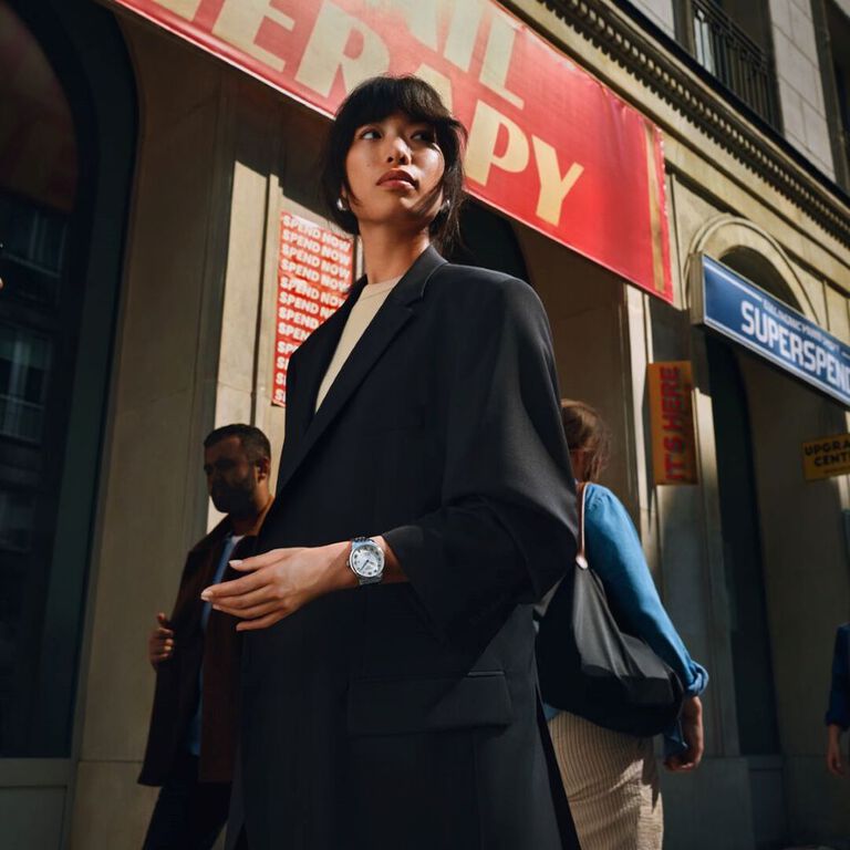 La montre Tissot Le Locle Powermatic 80 20th Anniversary Edition avec un bracelet en argent et un cadran bleu texturé, affichée sur un fond beige et rouge.