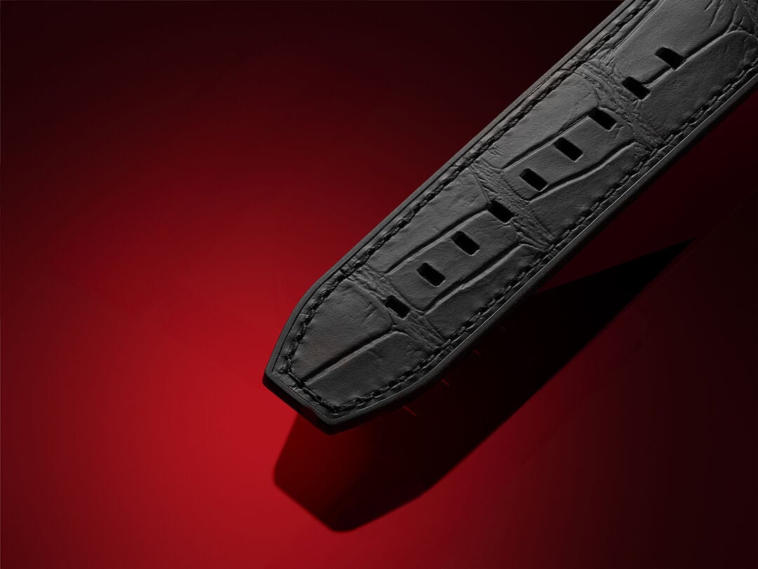 Close-up view of a black Tissot leather watch strap featuring an alligator-style texture and detailed stitching, set against a deep red background