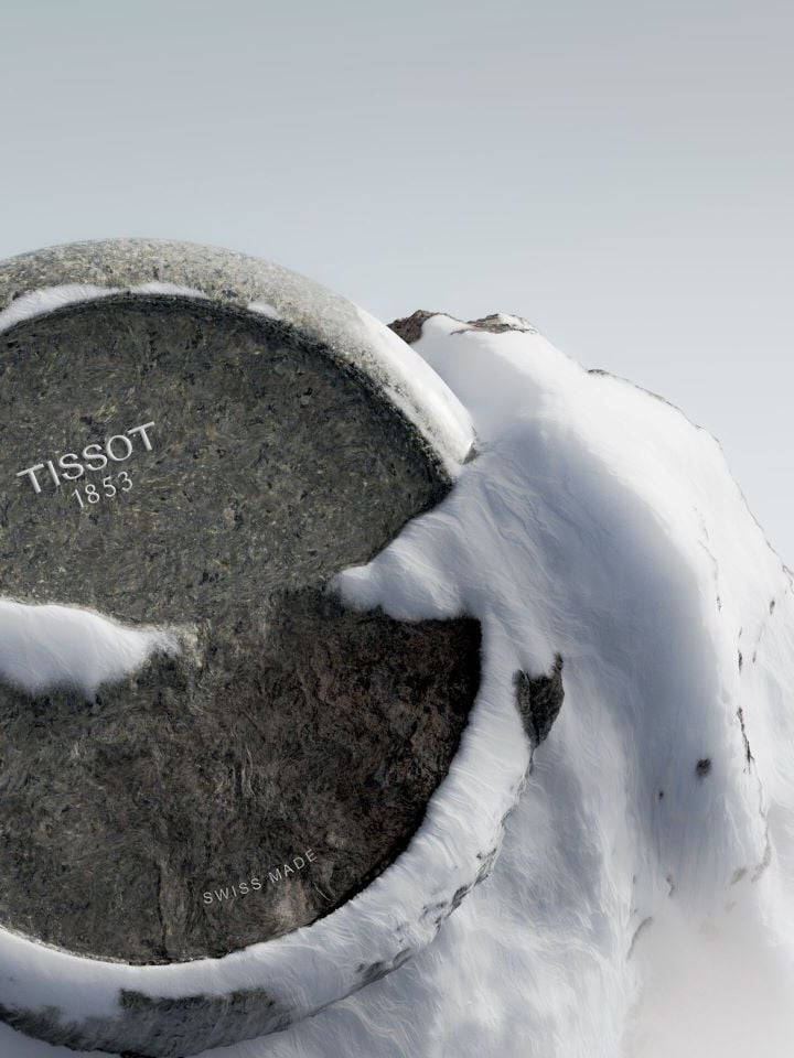 ティソ・ロックウォッチのケースが、スイスのユングフラウ山の雪に覆われた岩に埋め込まれ、ケースと背景の山頂にも雪が積もっている。