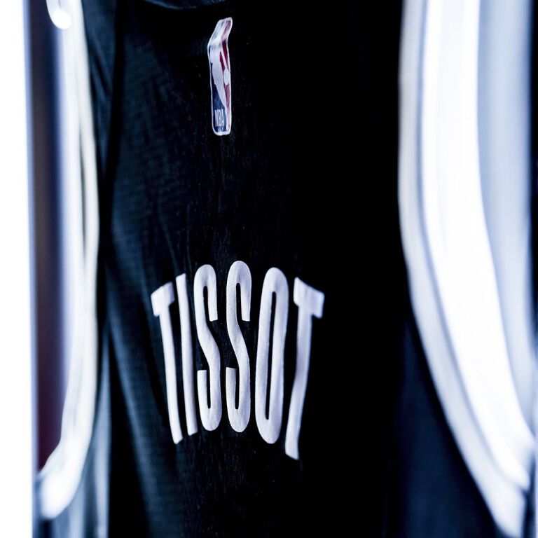 Image of the back of a blue and white basketball jersey bearing the Tissot name, number 04 and NBA logo.