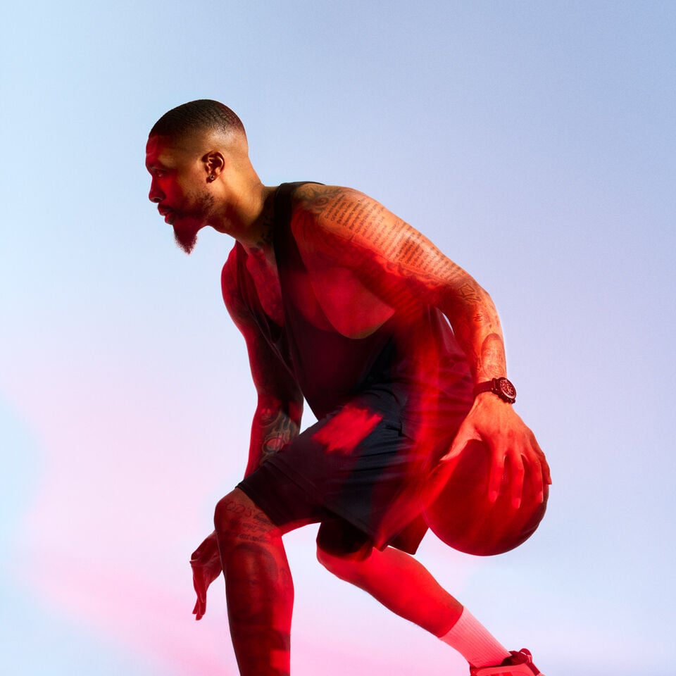 Damian Lillard, Tissot Ambassador, shown in profile mid-dribble, wearing dark athletic apparel and the Tissot NBA Supersport watch, highlighted by dramatic red lighting.