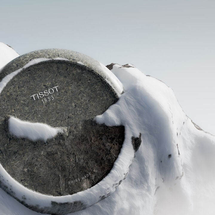 Close-up of a Tissot RockWatch dial carved from granite, partially covered in snow, with the inscriptions “Tissot 1853” and “Swiss Made” visible