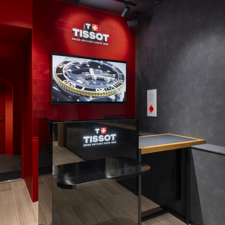 日本・大阪のティソ ブティックのカウンターで、カウンターには光るロゴがあり、ブランドカラーの赤い壁にも光るロゴが飾られている