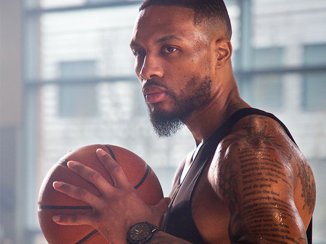 Damian Lillard posant de profil tenant un ballon entre ses mains et portant une montre Tissot