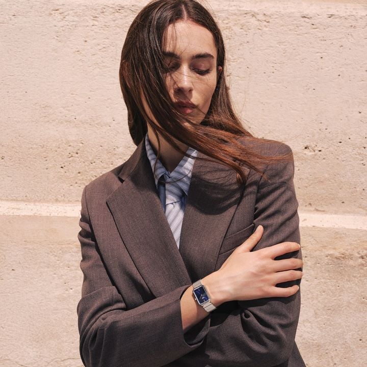 Tissot SRV stainless steel watch with blue dial, worn by a model in a tailored suit against a stone wall backdrop.