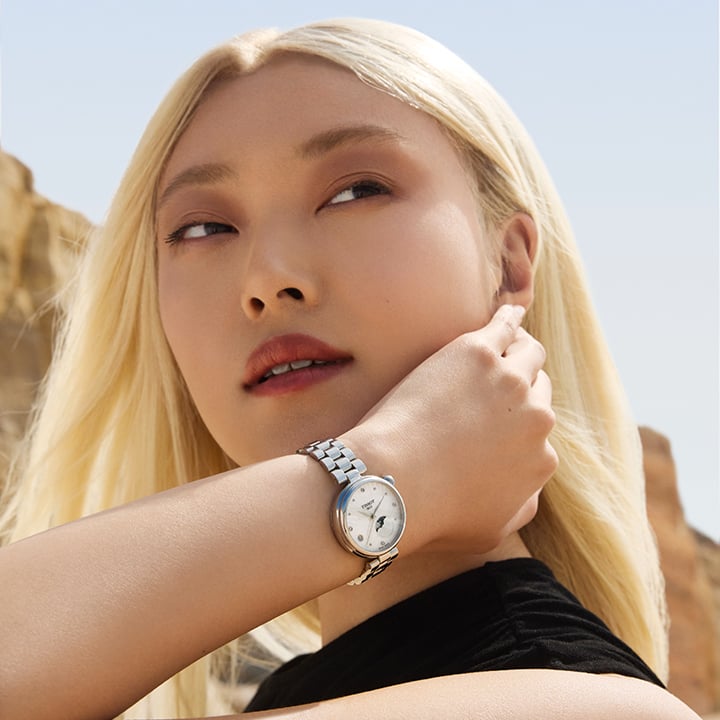 Blonde woman wearing the Tissot D&eacute;sir Moonphase watch on her wrist in a sunlit outdoor setting