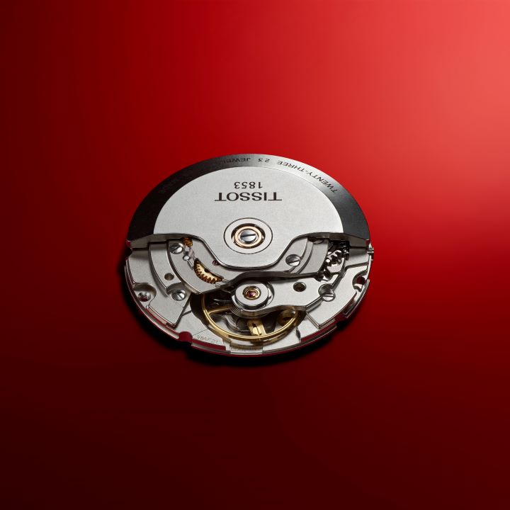 Close-up of the Tissot Classic Dream Powermatic 80 watch movement, showing the mechanical details, on a red background.