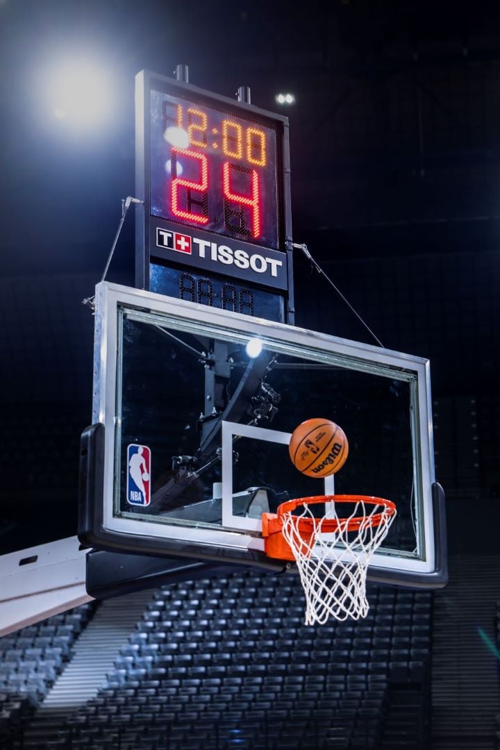 A Tissot-branded NBA shot clock displaying time, with a basketball mid-air approaching the hoop. 
