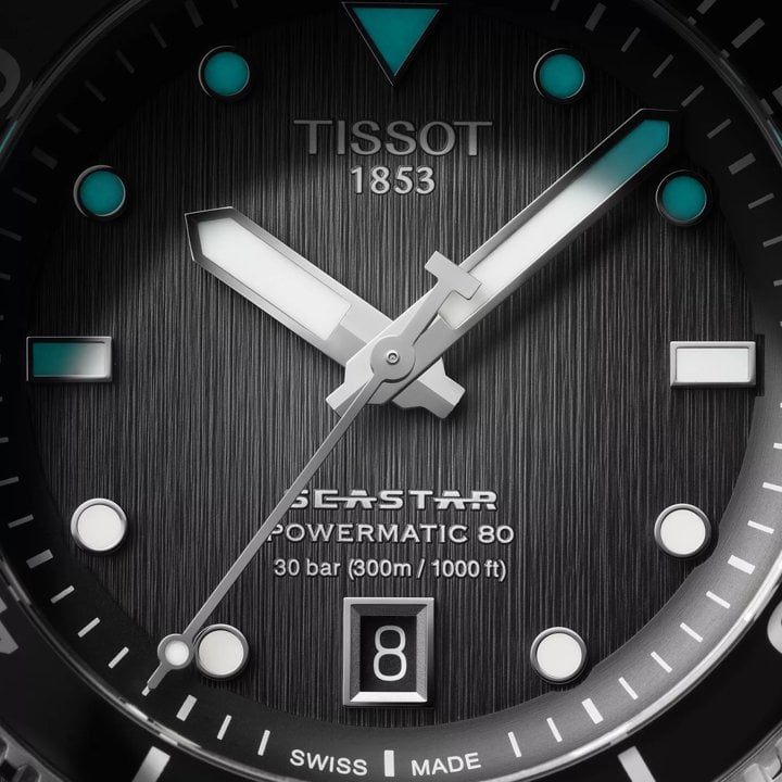 Zbliżenie na szary cyferblat Tissot Seastar 1000 Powermatic 80 40mm oraz technologię Superluminova, zapewniającą widoczność w słabym świetle.