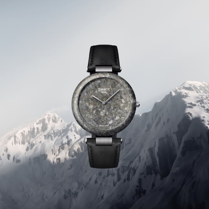 Tissot Rockwatch in the foreground with a black strap, against a backdrop of snow-covered mountains.
