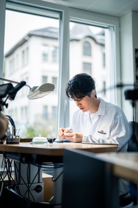 Lee Dong Wook carefully working on a watch at a Tissot workstation, dressed in a Tissot-branded lab coat. 