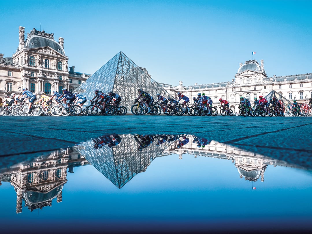 Riders cycling in front of the pyramide du Louvres, illustrating the sporting partnership between Tissot and the Tour de France