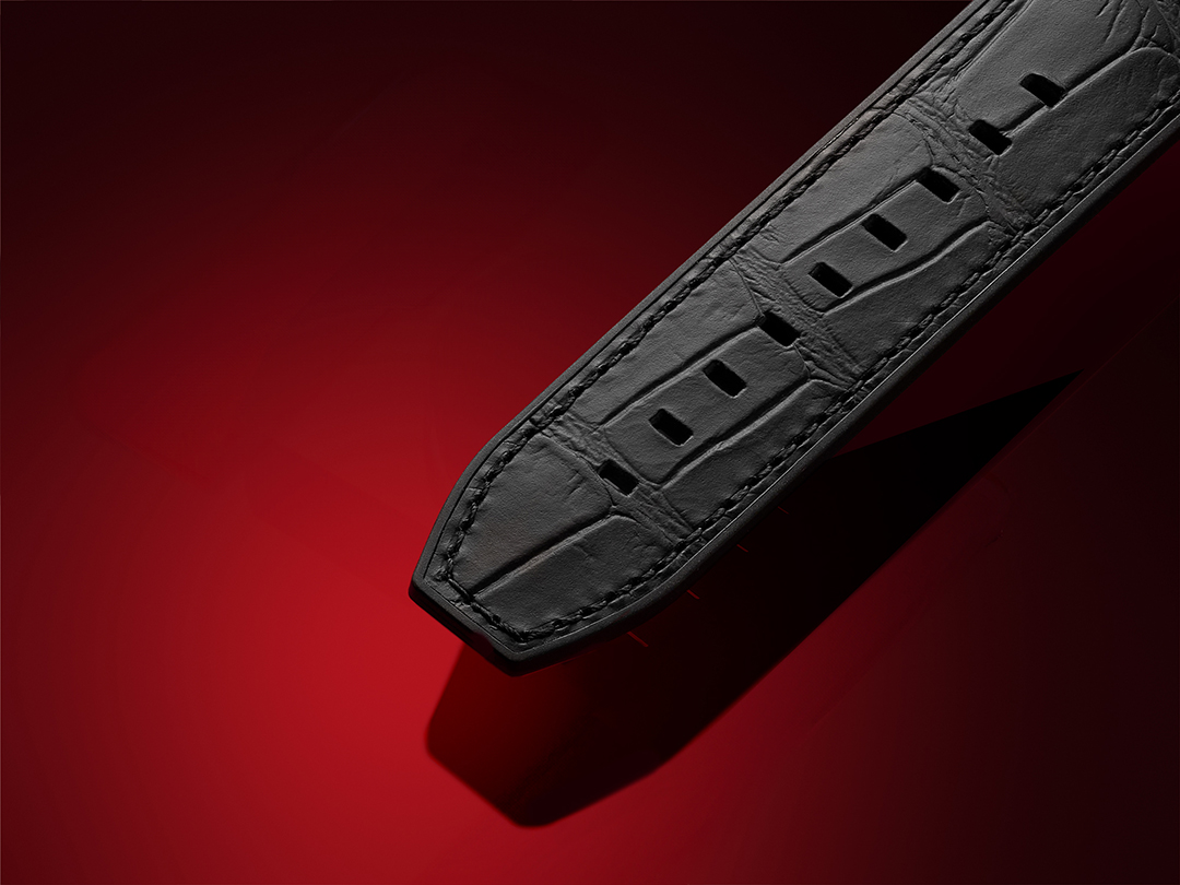 Close-up view of a black Tissot leather watch strap featuring an alligator-style texture and detailed stitching, set against a deep red background