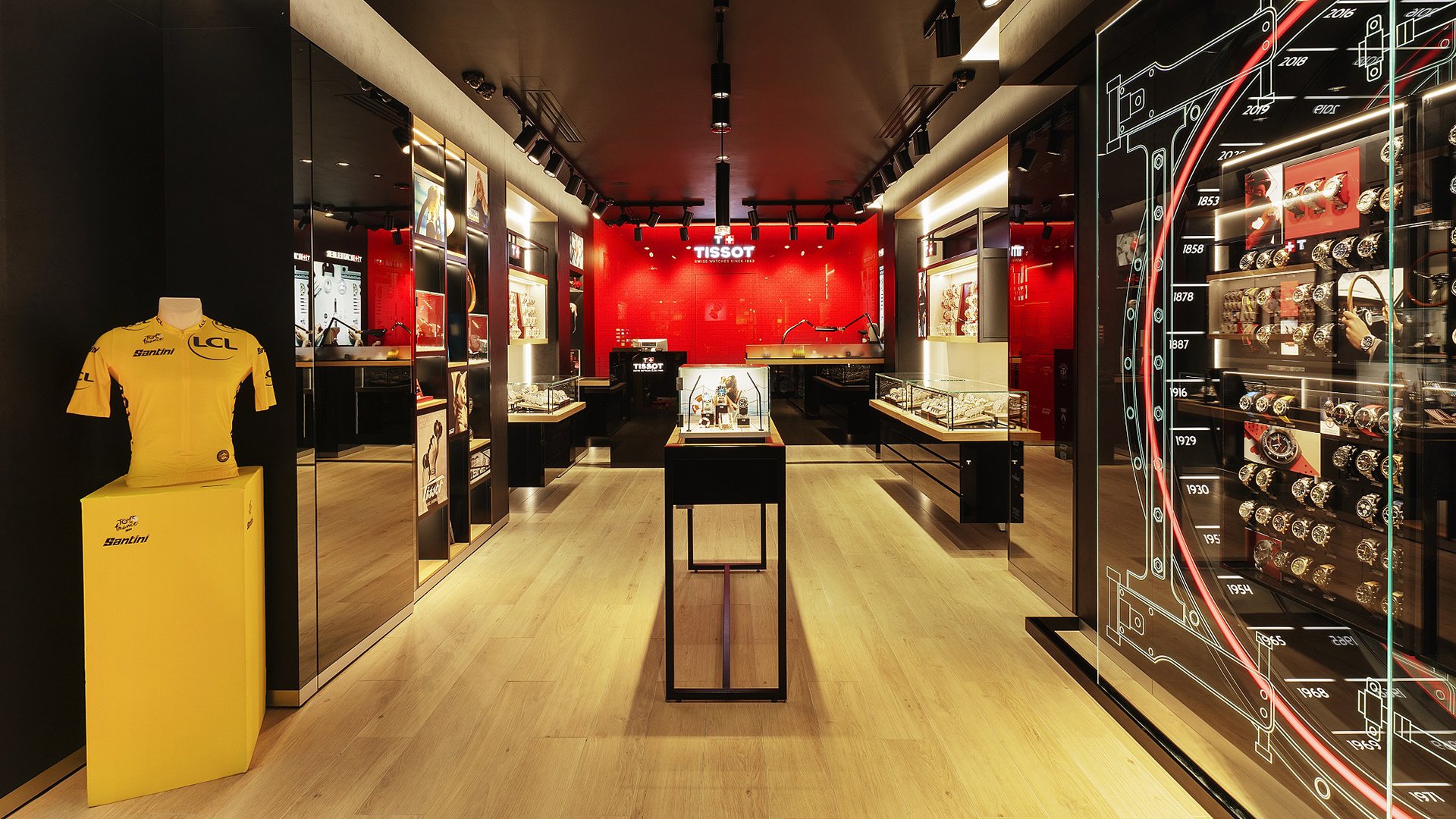 Interno della boutique Tissot, con espositori di orologi, una maglia gialla del Tour de France e elementi di design eleganti in nero e rosso.