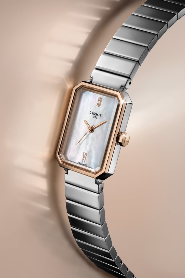 Close up of a Tissot SRV watch with a stainless steel case and bracelet, a rose gold bezel and a mother of pearl dial