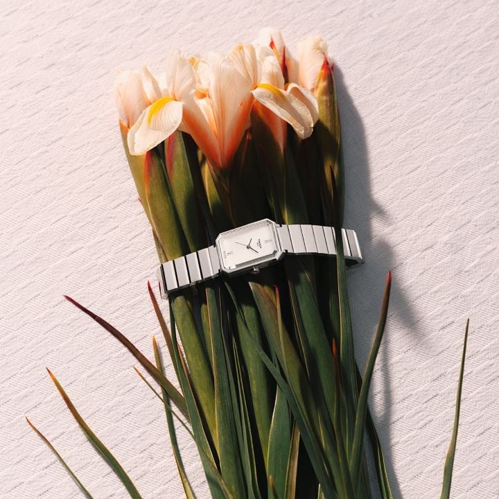 Tissot SRV stainless steel watch with grey dial, placed on a bouquet of pale flowers on a light textured fabric.