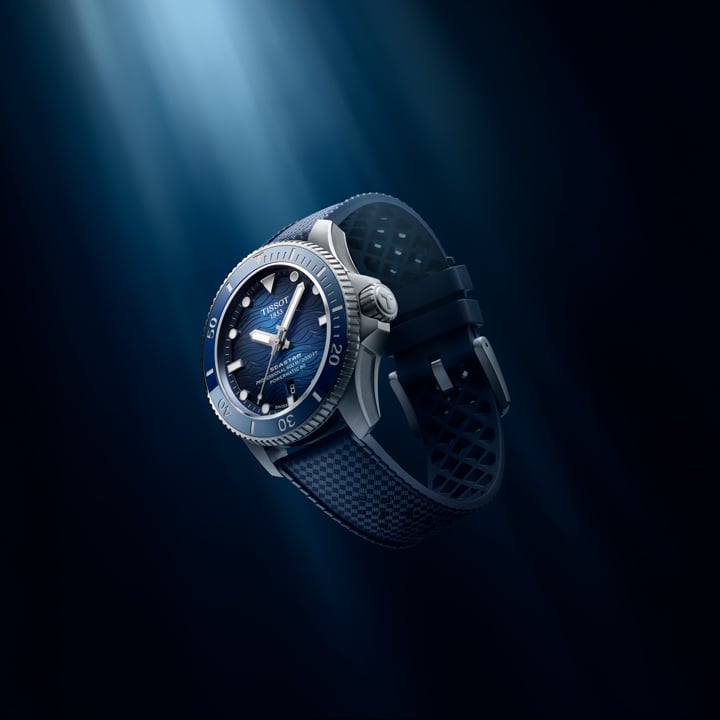 Blue Tissot Seastar diving watch with a textured rubber strap, illuminated underwater against a dark blue background.