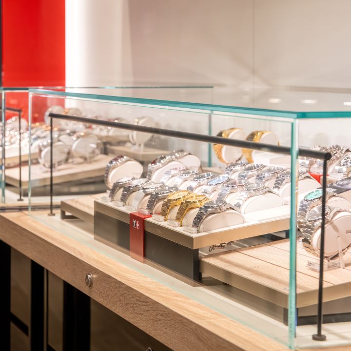 Een close-up van een glazen vitrine waarin verschillende Tissot-horloges worden tentoongesteld, waaronder zilveren en gouden modellen.