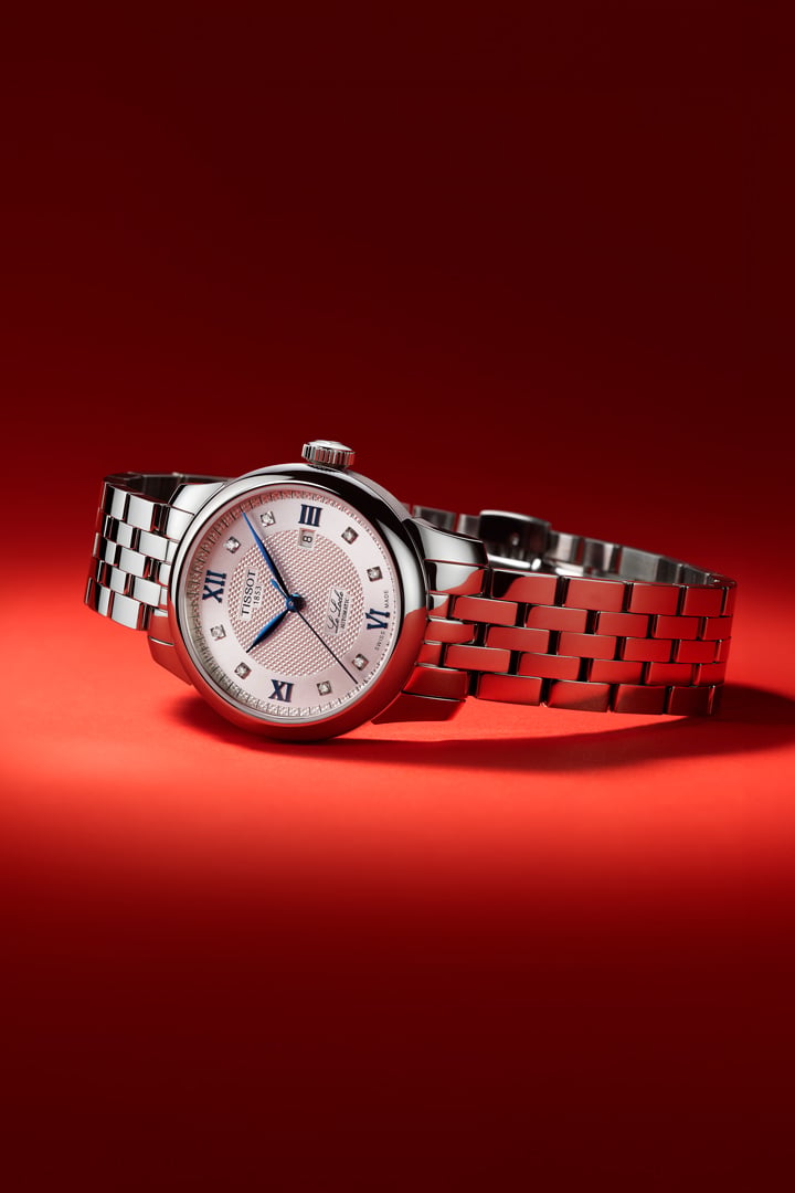 Montre Tissot Le Locle tout en acier avec cadran serti de diamants pos&eacute;e sur le c&ocirc;t&eacute; sur un fond rouge