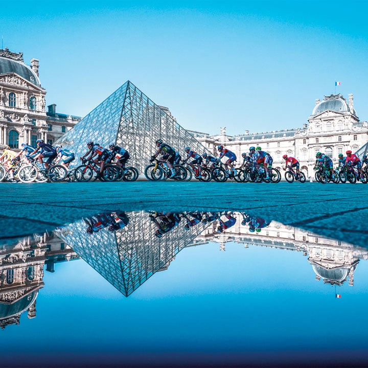 Professional cyclists riding next to the Louvre's pyramid