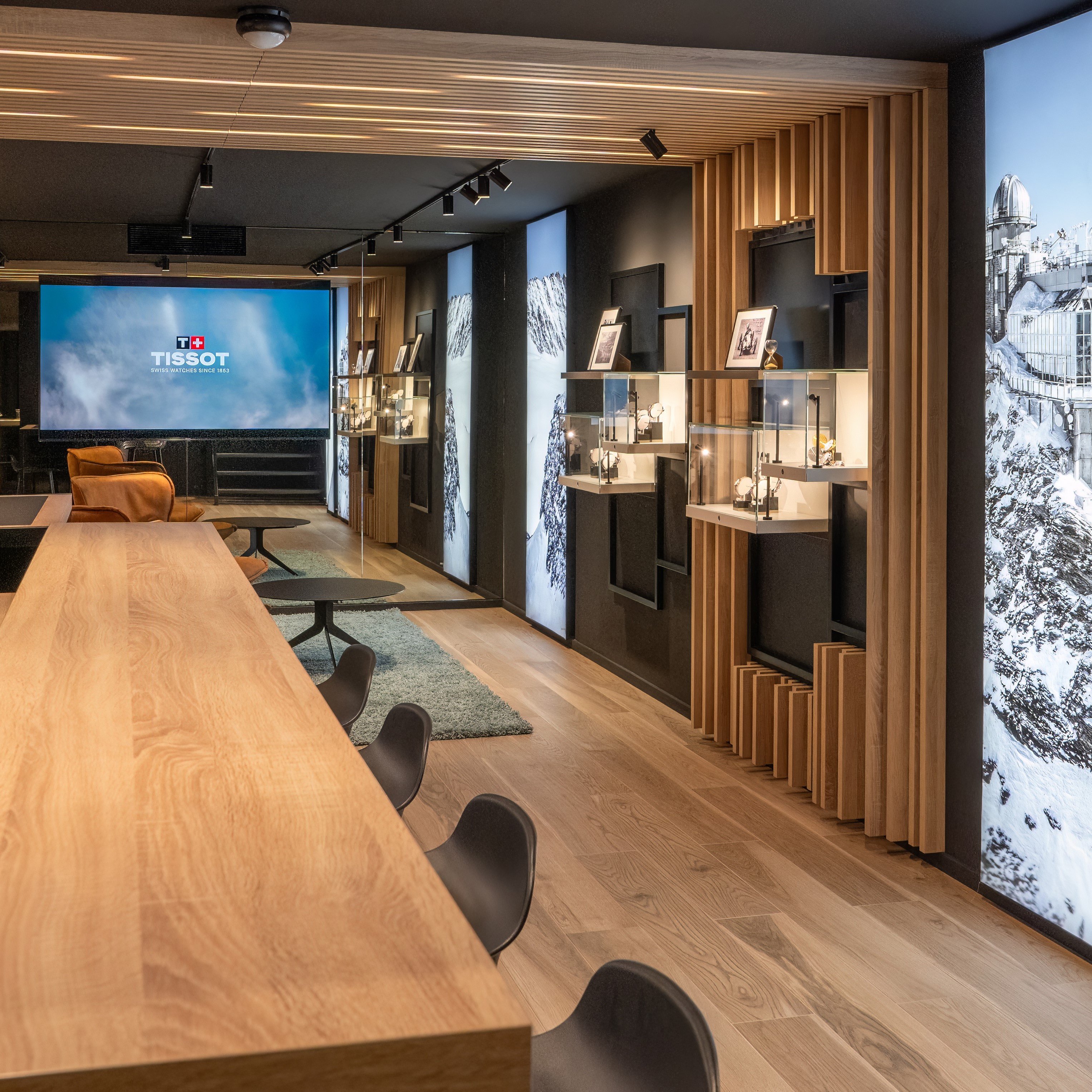 Een gezellige en moderne binnenruimte in de Tissot-boutique in Amsterdam, met een lange houten tafel en zwarte stoelen.