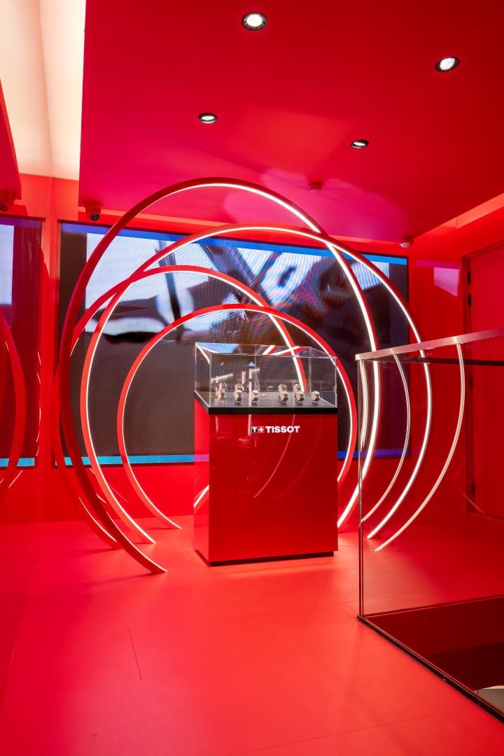Een gedurfde rode tentoonstellingsruimte in de Tissot-boutique, met een centrale glazen vitrine met een collectie horloges.