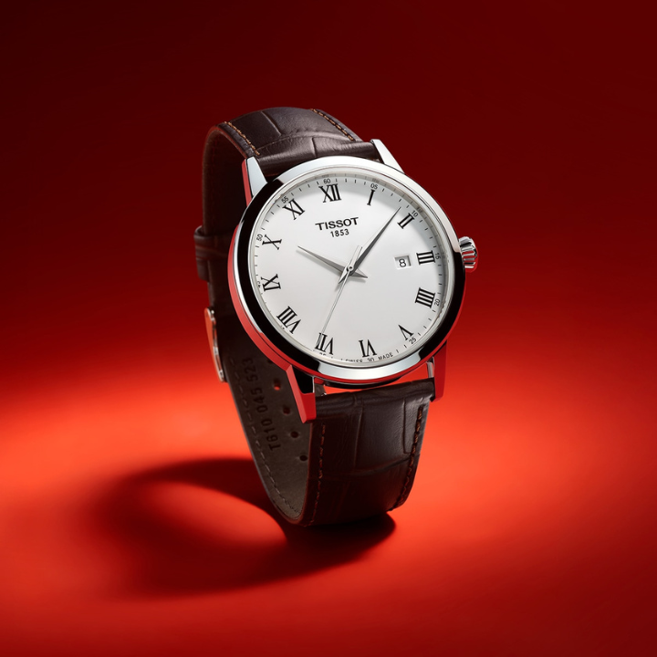 Tissot watch with Roman numeral dial and brown leather strap on a red background.